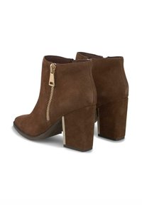 Botas de tobillo de ante marrón con un tacón grueso, que presentan un detalle de cremallera dorada en el lado y un diseño de punta redondeada.