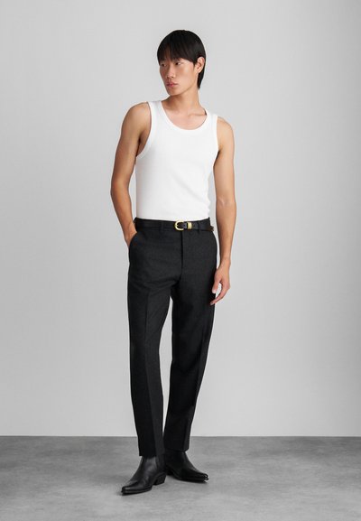 Camisola branca sem mangas combinada com calças cinza-escuro ajustadas, cinto de couro preto com fivela dourada e botins pretos.
