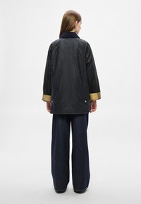 Fekete dzseki gallérral, arany színű díszítésekkel az ujjvégeken és laza szabással. Sötét, bő szárú farmerrel viselve. Simább textúrájú, hétköznapi kialakítás.