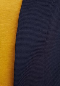 Gros plan sur un tissu texturé avec deux panneaux, l'un jaune doré et l'autre bleu marine foncé, montrant de fines lignes horizontales et un léger motif de tissage.