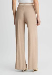 Pantaloni beige a gamba larga con una finitura testurizzata e una vita in contrasto, caratterizzati da una silhouette morbida che si estende fino al pavimento.