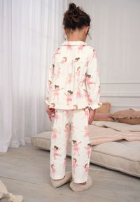 Pyjama pour enfants en tissu doux, avec un fond blanc orné d'imprimés ballerines roses. Comprend des manches longues et un pantalon, avec une coupe ample.