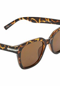 Lunettes de soleil en écaille de tortue avec des verres marron, design angulaire et accents en métal argenté aux charnières. Les montures texturées renforcent l'attrait visuel.