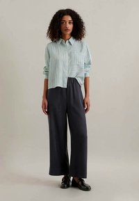 Ανοιχτό μπλε και λευκή ριγέ πουκάμισο με τσέπη στο στήθος, σε συνδυασμό με φαρδιά σκούρα γκρι παντελόνια και μαύρα παπούτσια.