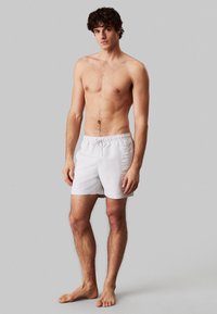 Pantaloni da mare bianchi con vita elastica e cordoncino, dotati di stampa del logo laterale. Tessuto liscio, design di lunghezza fino a metà coscia.