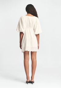 Weißes Baumwollkleid mit Puffärmeln, geraffter Taille und gewelltem Saum. Verziert mit Blumenstickerei.