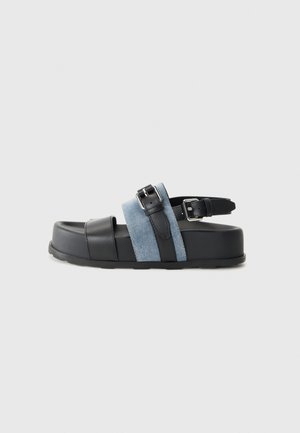 Sandalia negra y azul con una plataforma gruesa, material de cuero y denim, hebilla ajustable y diseño de punta abierta.