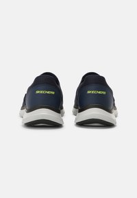 Tengerészkék tornacipők hálós felsőrésszel, fehér középtalppal és fekete talppal. A "SKECHERS" logó lime zöld színben látható, valamint texturált sarokrész jellemzi.