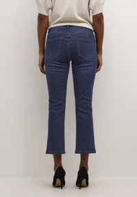 Mörkblå denimjeans med rak benmodell, fransad fåll och två bakfickor. Bärs med svarta högklackade skor.