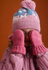 Różowa dziergana czapka z pomponem i motywem jednorożca. Grube różowe rękawiczki z ściągaczami. Zimowy płaszcz dla dziecka w miękkim różowym kolorze. Ciepłe tekstury.