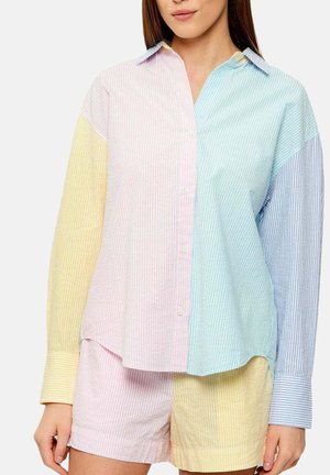 Vrouw draagt een pastel colourblock gestreept overhemd met knopen en bijpassende korte broek met gele, roze, blauwe en groene panelen.