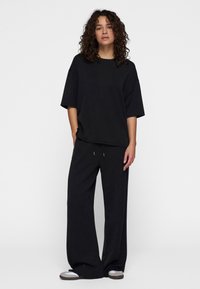 Zwarte oversized t-shirt en losse zwarte broek, beide gemaakt van zachte stof. Heeft ontspannen mouwen en een verstelbare taille met een trekkoord.