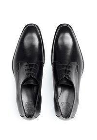 Chaussures habillées en cuir noir avec une texture lisse, bout rond et design classique à lacets. Présente un logo en relief sur la semelle intérieure.