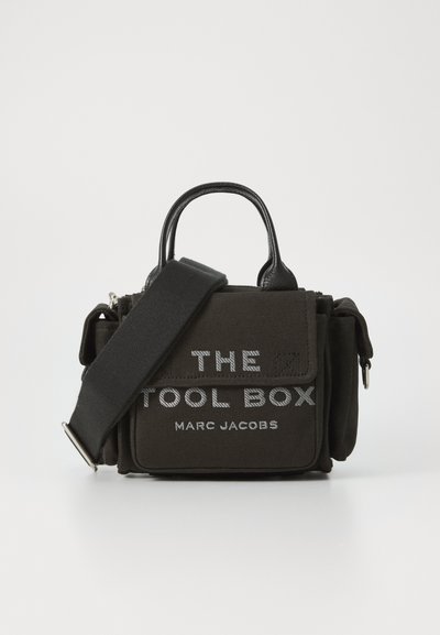 Zwarte canvas handtas met leren accenten, rechthoekige vorm, bovenhandvatten, afneembare schouderband, met witte tekst "THE TOOL BOX" en "MARC JACOBS."