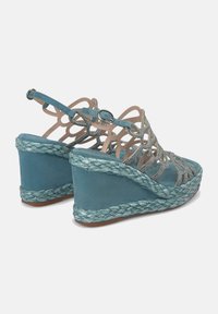 Sandalias de cuña en color aqua con suela de cuerda trenzada, que presentan un diseño de tiras entrecruzadas adornadas con strass y una correa en el tobillo trasero.