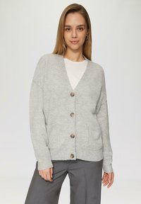 Graue Strickjacke mit V-Ausschnitt, fünf Holzknöpfen, Seitentaschen und langen Ärmeln, getragen über einem weißen Hemd und grauen Hosen.