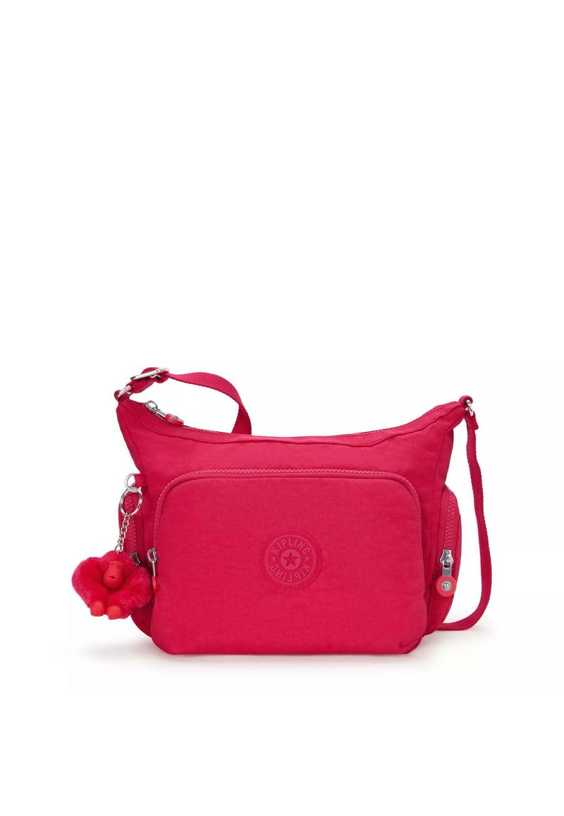 Pink fabric crossbody bag with a textured surface, a front zip pocket, a logo patch, and a fuzzy monkey keychain attachment.