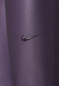 Legginsy sportowe Nike w ciemnofioletowym kolorze, wykonane z gładkiego materiału, z czarnym logo swoosh i wyraźnymi detalami szwów.