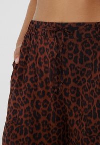 Pantalones de estampado de leopardo marrón hechos de tela suave, con una cinturilla elástica con cordón y bolsillos laterales para mayor comodidad.