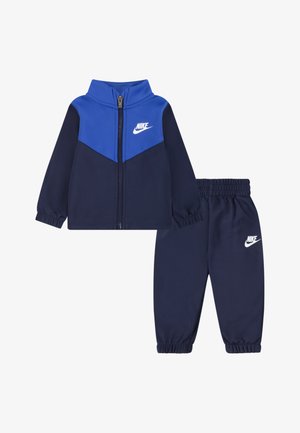 Trening albastru marin cu accente albastre. Jacheta cu fermoar are guler înalt și manșete elastice. Pantalonii au talie elastică și manșete, cu detalii de logo.