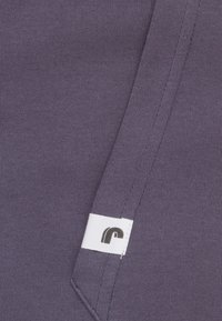 Paarse stof met een gladde textuur heeft een wit label met een zwart logo. Bevat een naaddetail langs één rand.