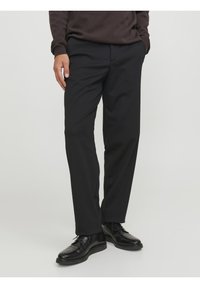 Pantalones negros de tejido suave, con corte recto, bolsillos laterales y combinados con zapatos negros brillantes.