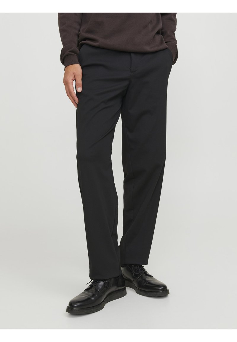 Pantalones negros de tejido suave, con corte recto, bolsillos laterales y combinados con zapatos negros brillantes.