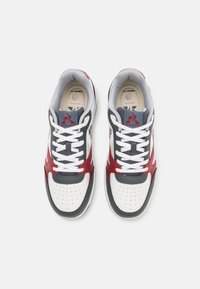 Sneaker bianche con accenti rossi e grigi, materiali in pelle e tessuto, punta perforata, collo imbottito e lacci piatti.