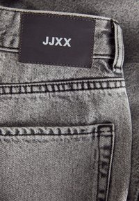 Szürke farmernadrág, a deréknál "JJXX" felirattal ellátott barna bőr címkével. Diszkrét varrás és hátsó zsebbeli design jellemzi.