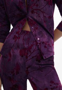 Ensemble de chemise et pantalon à motif floral violet, avec une finition texturée, des fermetures à boutons, des manches courtes et une taille élastique.