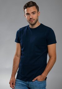 Marineblauwe katoenen t-shirt met korte mouwen, ronde hals en een gladde textuur. G gedragen met lichtblauwe jeans tegen een neutrale achtergrond.