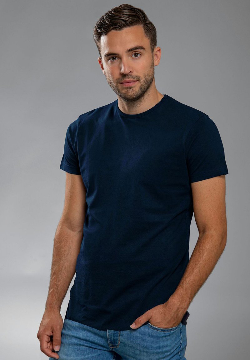 Marineblauwe katoenen t-shirt met korte mouwen, ronde hals en een gladde textuur. G gedragen met lichtblauwe jeans tegen een neutrale achtergrond.