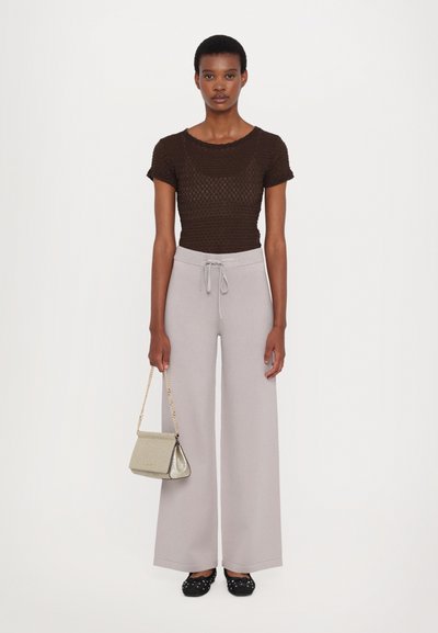 Brown patterned knit top, light gray wide-leg trousers, black shoes with white polka dots, and a small glittery handbag with a chain strap.