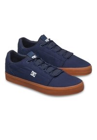 Granatowe trampki z płótna na niskim profilu z brązową gumową podeszwą, wyposażone w sznurowadła, wyściełany kołnierz i akcent z logo po boku.
