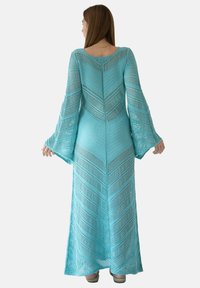 Długa, zwiewna sukienka w turkusowym, dzianinowym materiale z wzorem w zygzaki, charakteryzująca się długimi rękawami w kształcie dzwonu oraz prostym tyłem.