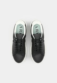 Sorte sneakers med en glatt overflate, hvit gummisåle og mintgrønn innersåle. Har snører og logo på sidene.