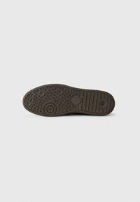 Suela de zapato de goma marrón con un patrón de agarre texturizado, con indentaciones circulares y un diseño segmentado para ofrecer tracción. Sin marcas visibles.