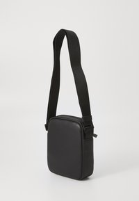 Sorte læder crossbody taske med firkantet form, tekstureret overflade, justerbar stofrem og minimalistisk design.