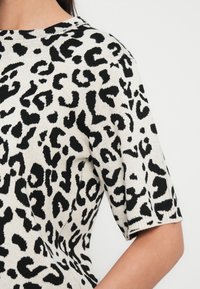 Πουλόβερ με λεοπάρ μοτίβο σε κρεμ και μαύρο, με υφή πλεξίματος, κοντά μανίκια και στρογγυλή λαιμόκοψη, που αναδεικνύει έντονο σχέδιο.