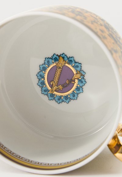 Λευκό πορσελάνινο φλιτζάνι με χρυσή στεφάνη και λαβή, διακοσμημένο με κεντρικό ανθικό έμβλημα με μπλε φύλλα και χρυστό και μοβ κυκλικό σχέδιο.