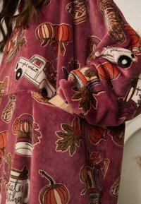 Pluche, roze kledingstuk met diverse herfstthema-afdrukken, waaronder pompoenen, bladeren en potten. Oversized pasvorm met een zachte textuur.
