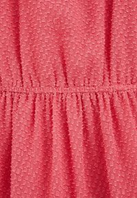 Tela color coral con un patrón texturizado, que presenta una cintura fruncida. La superficie tiene un diseño irregular y ligeramente en relieve.