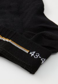 Schwarze gestrickte Socken mit einem strukturierten Muster. Der Bund hat weiße und gelbe Nähte mit einer numerischen Detail.