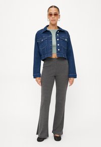 Jeans jakna skraćena s kopčanjem, svijetlozelena uska majica, rebraste sive široke hlače i crne balerinke, nosi se uz naočale s okruglim okvirom.