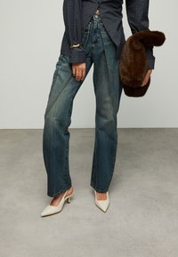 Blauwe spijkerbroek met hoge taille en wijde pijpen, met een uitgebleekte wassing. Gecombineerd met witte slingback pumps met puntige neus en een bruine clutch van bont.