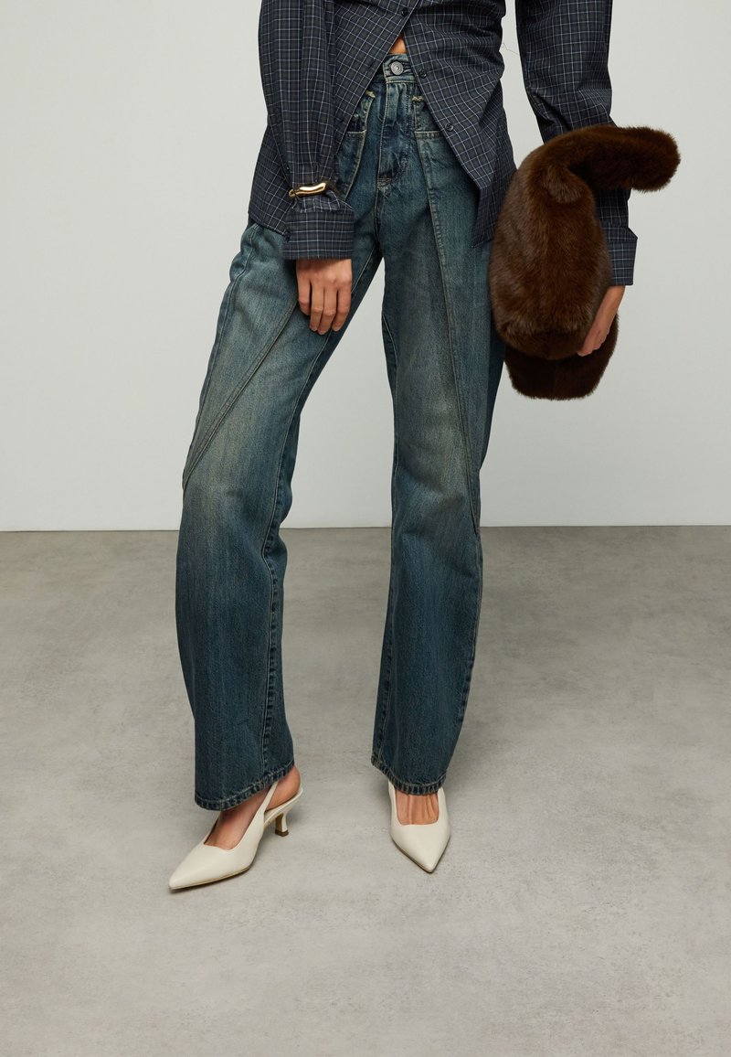 Blauwe spijkerbroek met hoge taille en wijde pijpen, met een uitgebleekte wassing. Gecombineerd met witte slingback pumps met puntige neus en een bruine clutch van bont.