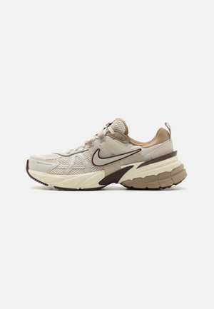 Beige en bruine Nike hardloopschoen met mesh bovenwerk, dikke gewatteerde zool en groot Swoosh-logo aan de zijkant.