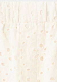Tissu ivoire avec motif brodé d’œillets et détail de couture froncée, créant un design texturé et aérien.