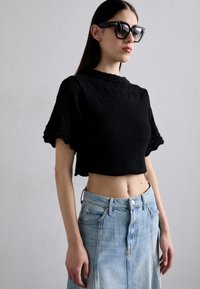 Top corto nero in maglia con maniche a scallop, abbinato a una gonna di jeans azzurri chiaro con chiusura a bottoni e tasche laterali.