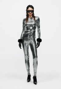 Silver sequin top and leggings with faux fur cuffs, black gloves, and high-heeled shoes; fitted silhouette and reflective texture.